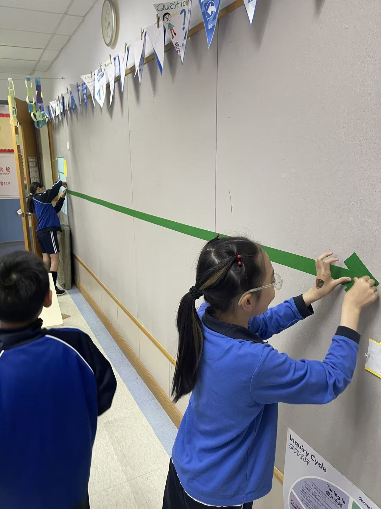 Two students taping a long green timeline arrow across a mostly empty classroom wall